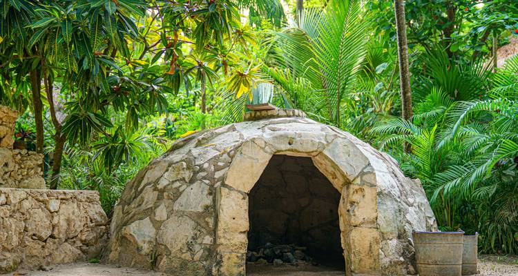 Aus Stein erbautes, kuppelförmiges Schwitzbad, eingebettet in üppiges Dschungelgrün und Palmwedel.