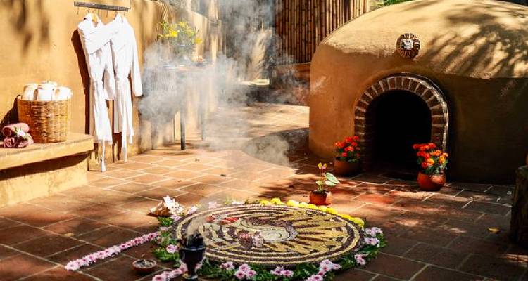 Temazcal-Eingang mit dekorativem Blumenmandala und aufsteigendem Räucherwerk in einem rustikalen Innenhof.