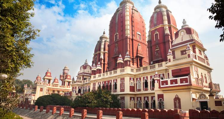 Large cream and red Hindu temple complex with ornate towers rising into a partly cloudy sky.