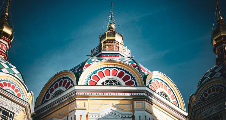 Close-up upward view of the colorful domes and spires of Zenkov Cathedral against a deep blue sky.