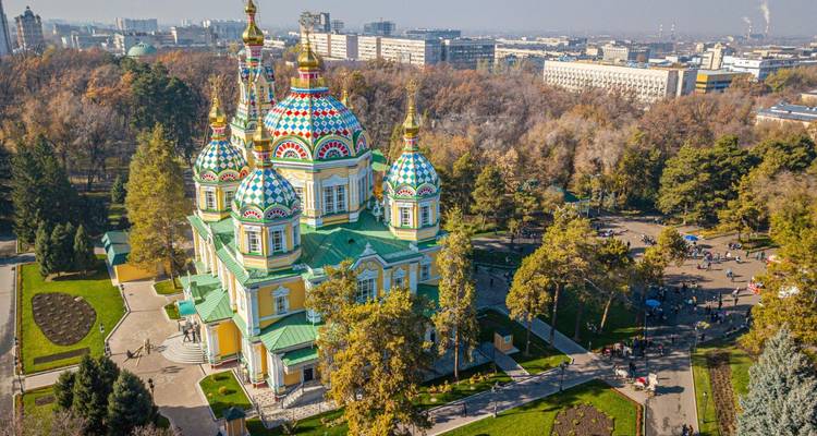Aerial view of brightly colored Zenkov Cathedral surrounded by autumn trees and a cityscape beyond.