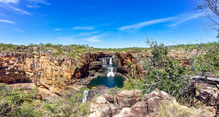 Dramatic tiered waterfall plunging into deep pool between rugged red rock cliffs