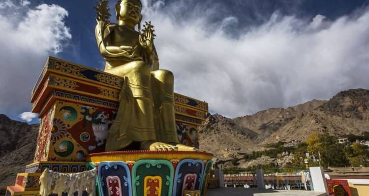 Huge golden seated Buddha statue atop a vividly painted pedestal with rugged mountains behind.