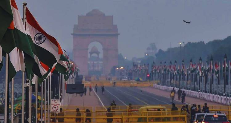 India Gate boulevard lined with national flags and security barriers in hazy early morning light.