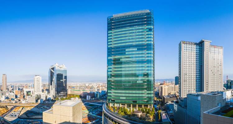 Les tours gratte-ciel modernes dominent l'horizon lumineux d'Osaka sous un ciel bleu dégagé.