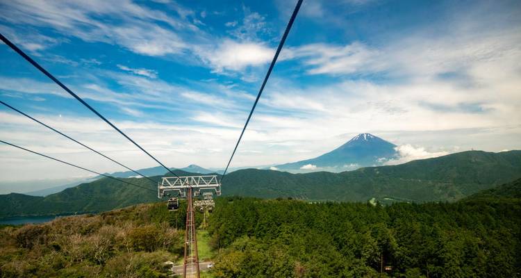 Survol en téléphérique au-dessus de montagnes boisées en direction du Mont Fuji aux pics enneigés lors d'une journée claire