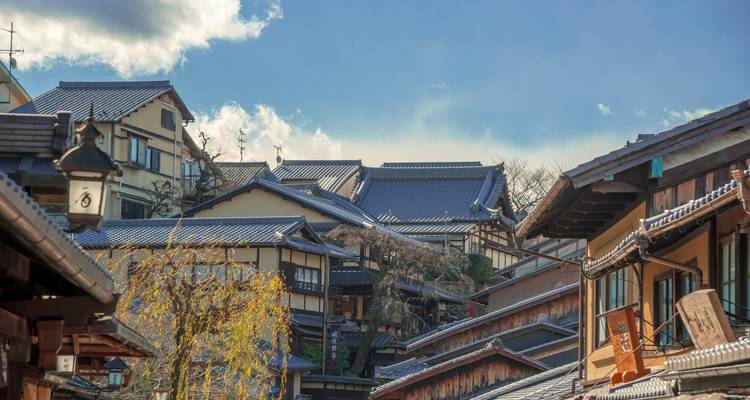 Des rangées de maisons de ville en bois traditionnel s'élèvent le long d'une ruelle étroite de Kyoto sous un ciel bleu
