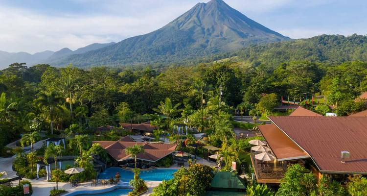 Complexe hôtelier avec piscines au pied du majestueux volcan Arenal sous un ciel dégagé