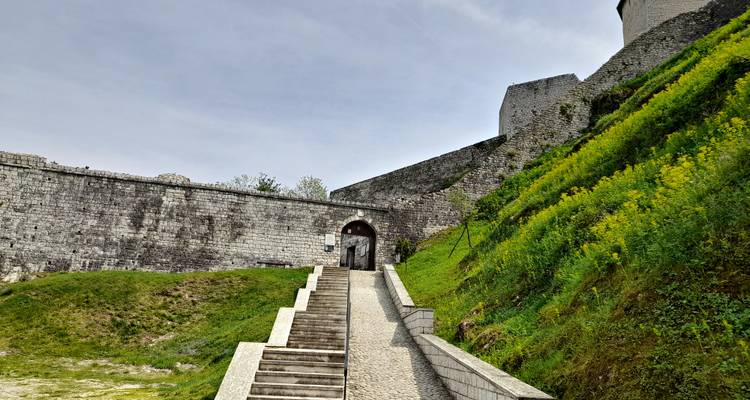 Un long escalier menant à un immense mur de forteresse en pierre établi contre un talus verdoyant.