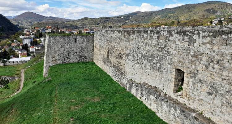 Les longs remparts de pierre d'une forteresse s'étendant sur une crête herbeuse avec des vues sur la ville au-delà.