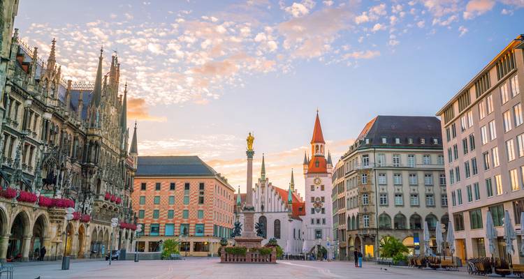 Vroeg ochtendlicht dat Münchens Marienplatz baadt, met bloemrijke bogen en kerktorens onder een gespikkelde hemel.