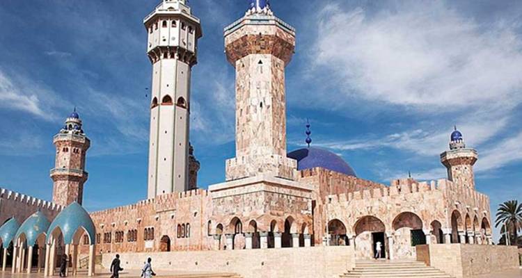 The marble-clad Great Mosque of Touba with soaring minarets against a bright blue sky.