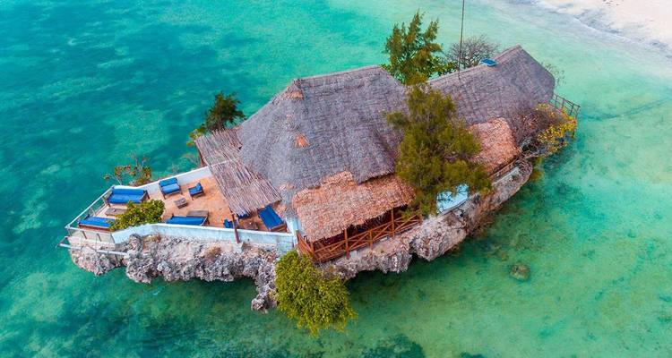 Aerial view of an over-water restaurant perched on a coral rock surrounded by turquoise sea.