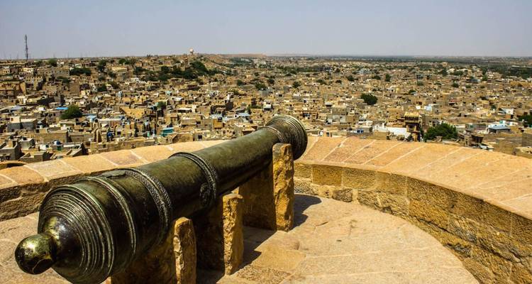 Historic cannon overlooking the vast sandstone cityscape of Jaisalmer from the fort ramparts.