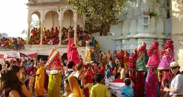 Vibrant street festival with crowds in colourful attire watching decorated dancers in front of a temple façade.
