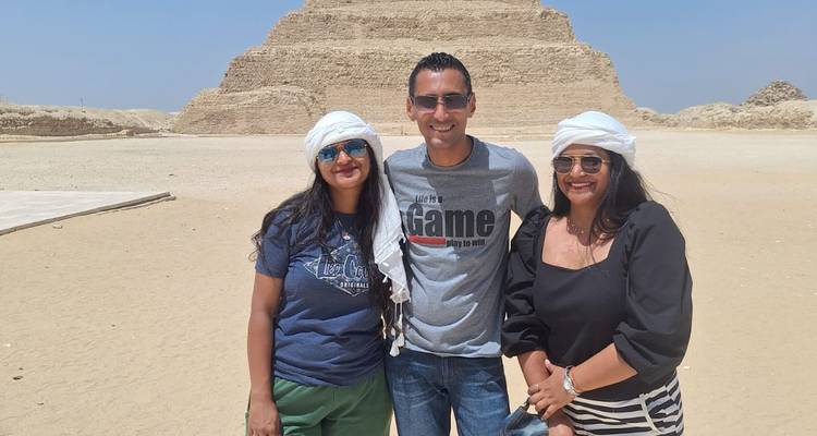 Trois voyageurs posant devant la Pyramide à Degrés par une journée désertique dégagée.