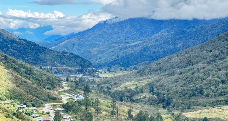 Vallée bhoutanaise verdoyante avec route sinueuse, rivière et villages dispersés sous des collines en étages.