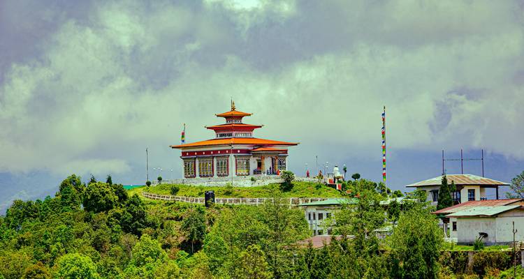 Temple en haut d'une colline aux couleurs vives encadré par une végétation luxuriante et des nuages spectaculaires au Bhoutan.