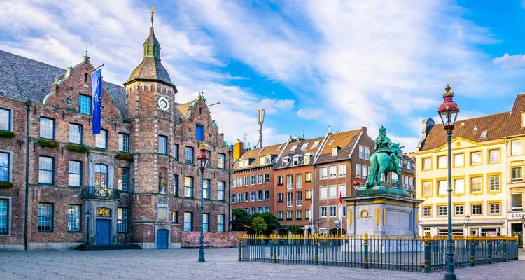 Historic Düsseldorf town square with brick Rathaus, equestrian statue and vibrant buildings under blue sky.