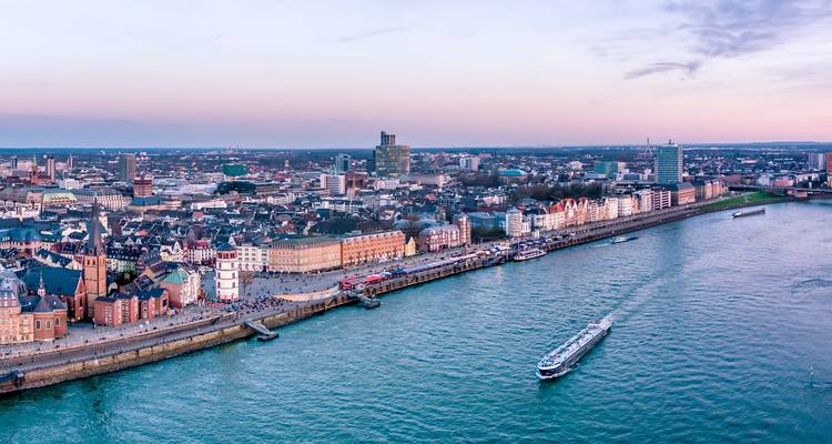 High-angle view of Düsseldorf skyline along the Rhine with cruise ship at dusk.