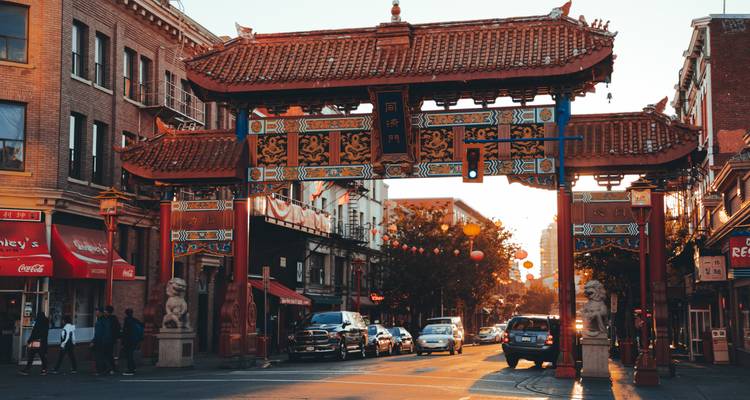 Ornate traditional gate marking a Chinatown street as cars and pedestrians pass in late afternoon light.