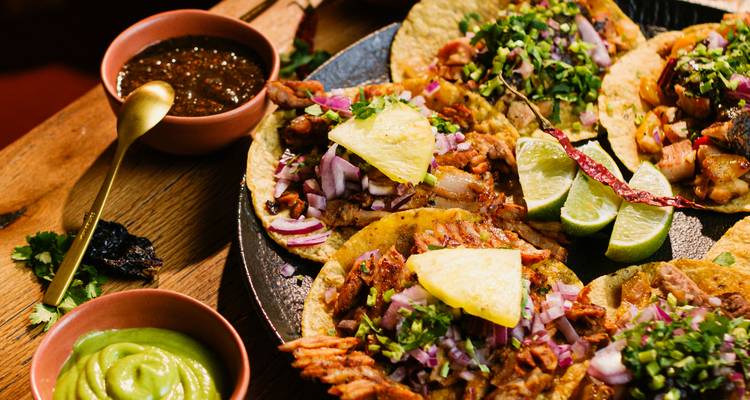 Platte mit frisch zubereiteten Tacos, garniert mit Ananas, Limettenscheiben und lebendigen Salsas auf einem Holztisch.