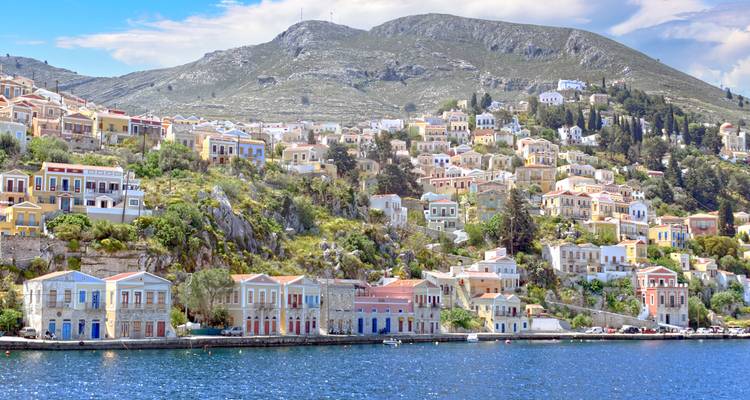 Farbenfrohe neoklassizistische Häuser erstrecken sich eine Hanglage hinunter zum glitzernden Hafen von Symi.