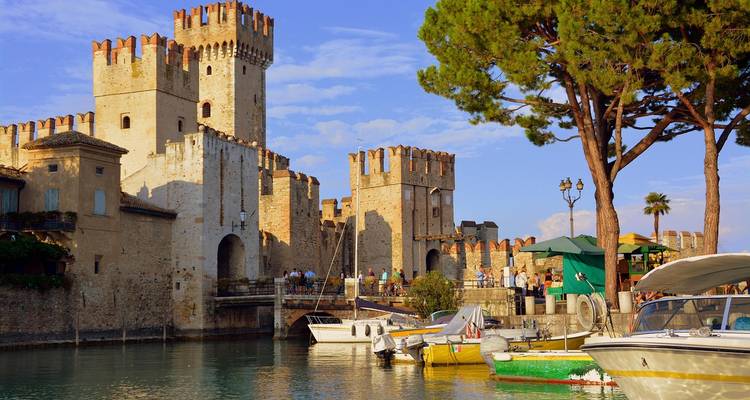 Medieval Scaliger Castle rising above a picturesque harbour with small boats on Lake Garda.