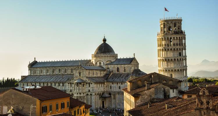 Iconic Leaning Tower and Pisa Cathedral bathed in warm evening light with Tuscan hills beyond.