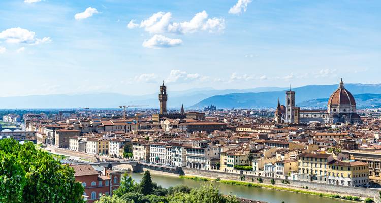 Expansive panoramic view of Florence skyline including the Duomo and Arno River under blue skies.