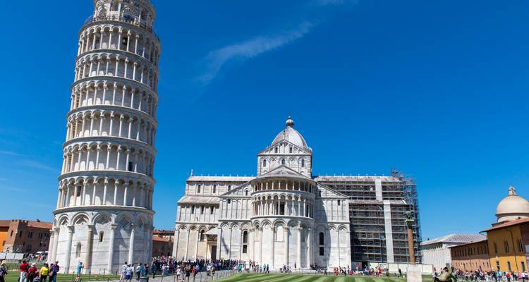 Crowds gather around Pisa’s Leaning Tower and cathedral complex on a bright blue-sky day.