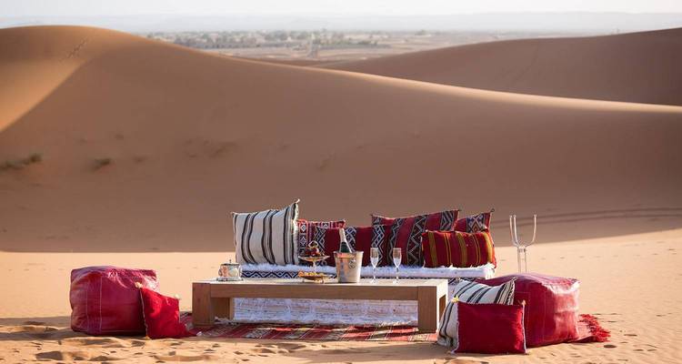 Mesa baja elegante con cojines lista para el té en las dunas doradas al atardecer