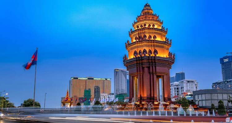 Illuminated Independence Monument in Phnom Penh at dusk with light trails from traffic.