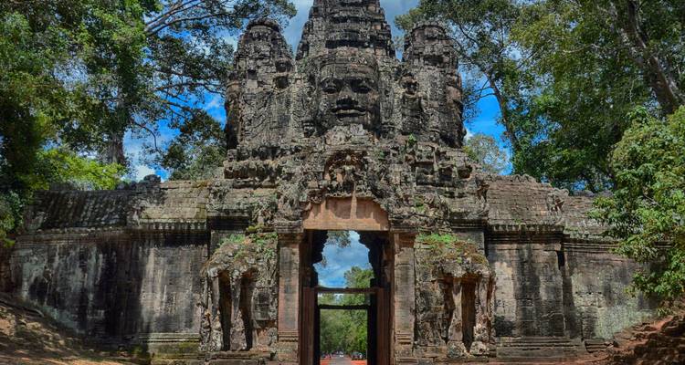 Stone gateway with serene Buddha faces at Angkor Thom surrounded by towering jungle trees.