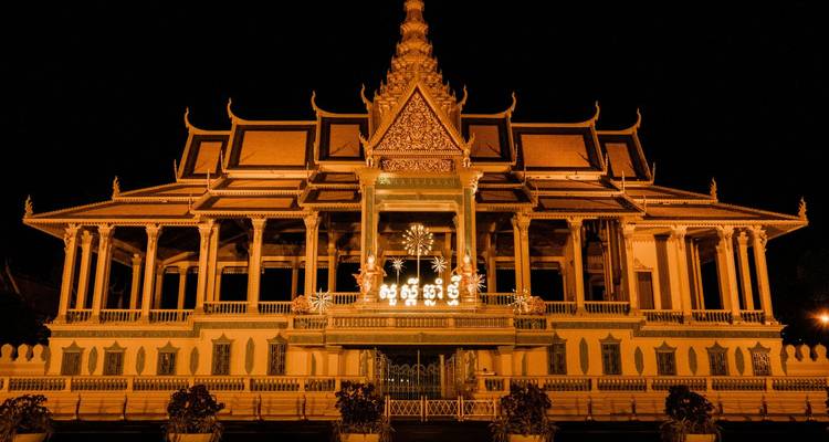 Nighttime illumination of Phnom Penh’s Royal Palace shining against a dark sky.