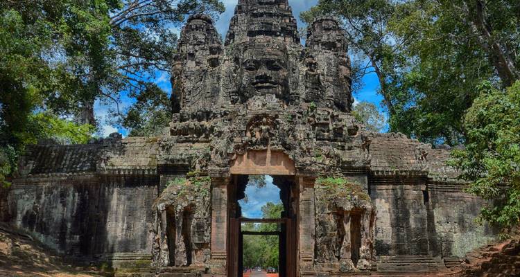 Porte de pierre d'Angkor Thom avec des visages sculptés sereins entourés par les arbres de la forêt tropicale imposants.