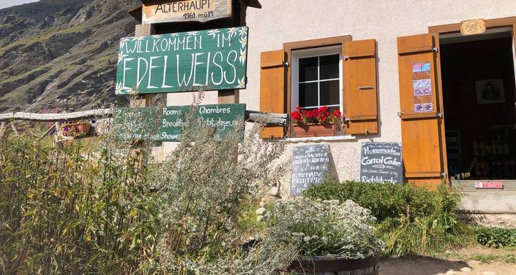 Entrée rustique de refuge alpin avec volets en bois et panneau de bienvenue allemand entouré d'herbes aromatiques.