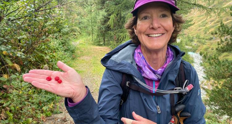 Randonneur souriant montrant une poignée de baies sauvages sur un sentier de montagne forestier.