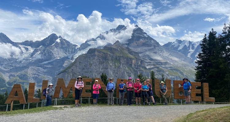 Grand groupe de randonneurs posant devant un panneau en bois avec les Alpes suisses spectaculaires en arrière-plan.