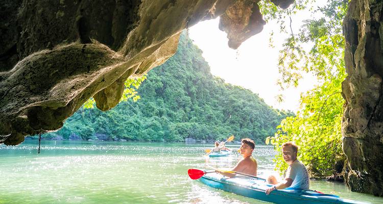 Vrienden kayakken onder kalkstenen kliffen en groen oerwoud in Halong Bay