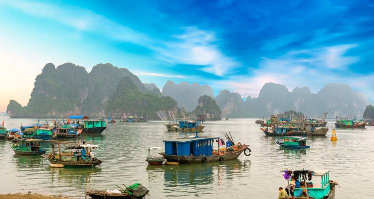 Traditionele vissersbootjes drijvend tussen dramatische kalksteeneilanden in Ha Long Bay onder een blauwe hemel