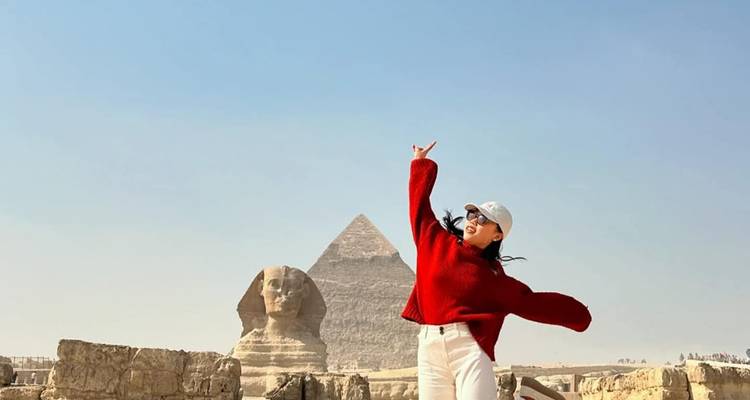 Una mujer con un suéter rojo hace una pose divertida con la Esfinge y una pirámide perfectamente alineadas detrás de ella.