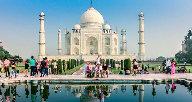 Visitors gather in front of the ivory-white Taj Mahal, perfectly mirrored in the long reflecting pool under a clear blue sky.