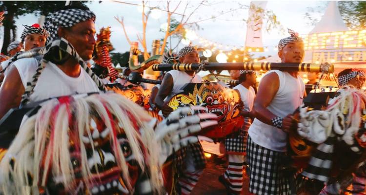 Traditional Balinese performers in colorful costumes carrying a dragon effigy during a lively night parade.