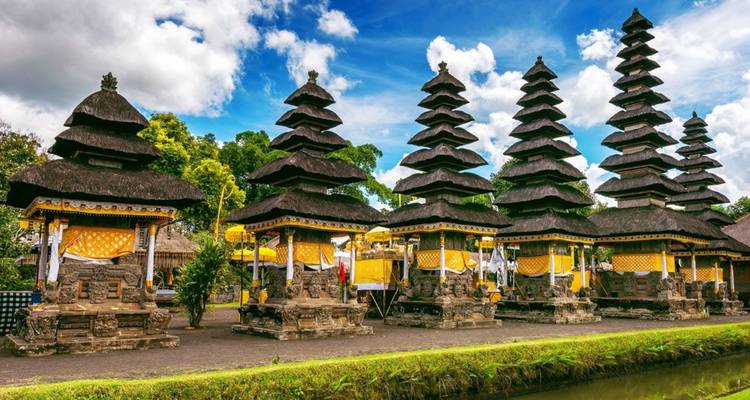 Row of multi-tiered pagoda-style temple shrines reflected in a narrow moat under a blue sky.