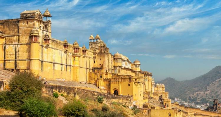 Die massiven gelben Sandsteinmauern des Amber Fort dominieren einen zerklüfteten Berghang unter blauem Himmel.