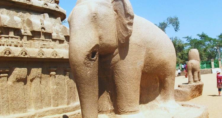 Stone sculpture of a life-size elephant beside ancient carved temple walls on a sunny day.