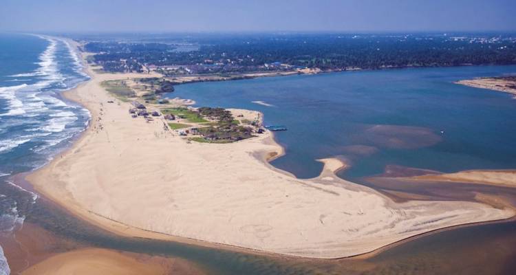 Aerial view of a sandy peninsula bordered by sea waves on one side and calm backwaters on the other.