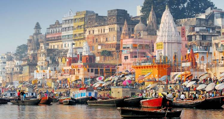 Colourful riverside ghats of Varanasi bustling with boats and pilgrims against a hazy sky.