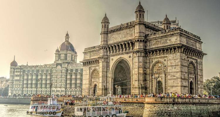 Iconic Gateway of India arch with the Taj Mahal Palace hotel behind and ferries in the harbour.